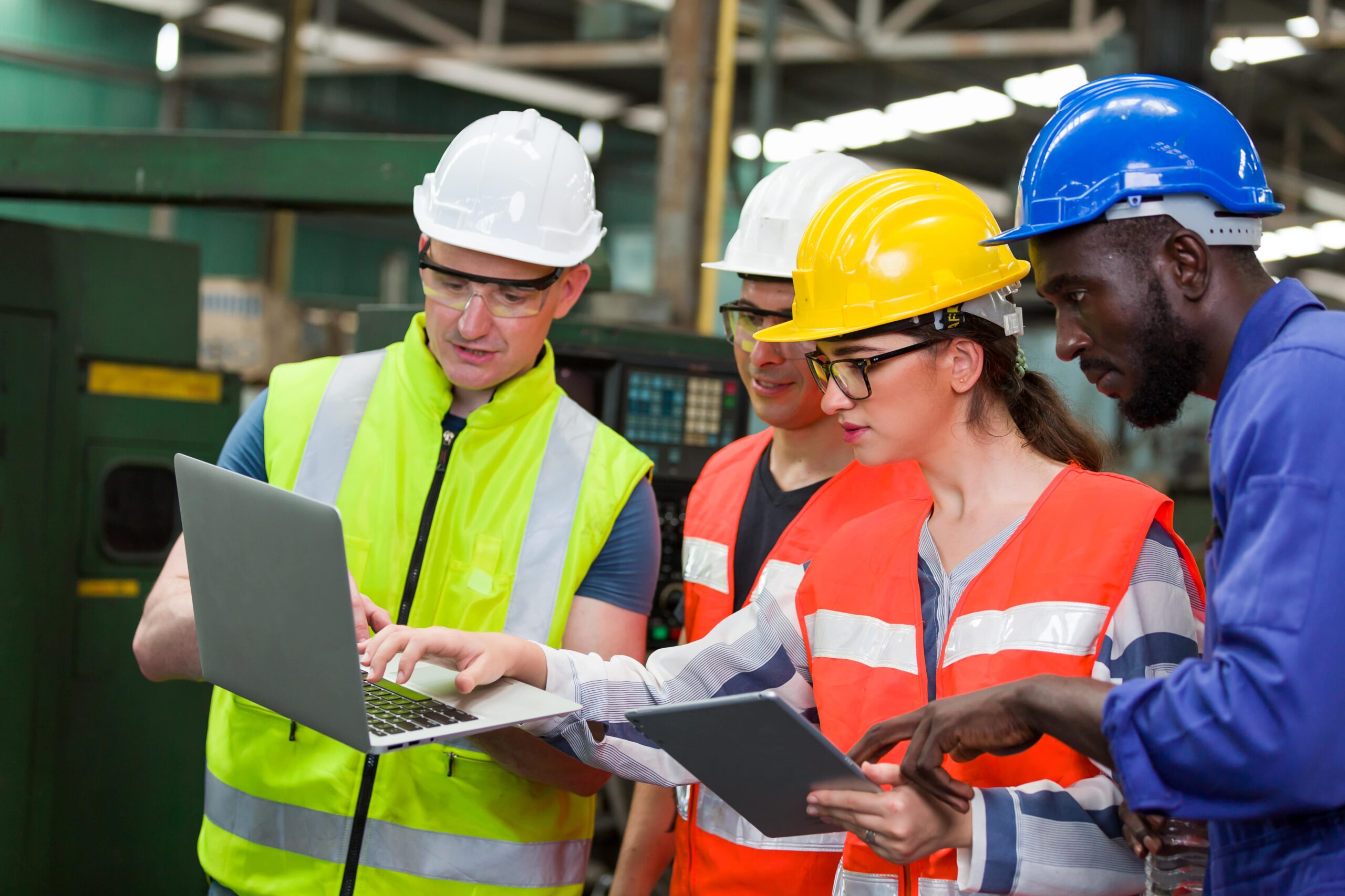site workers, wearing high-vis and hard hats reviewing report on a laptop, comparing it to a report on a tablet